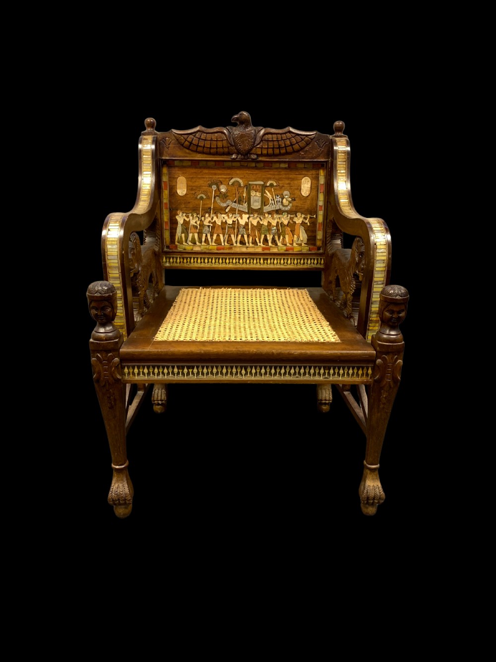 A three-piece nineteenth-century Egyptian Revival furniture suite consisting of a settee and two armchairs with carved winged crestings, figural marquetry backrests, and cane seats. View III