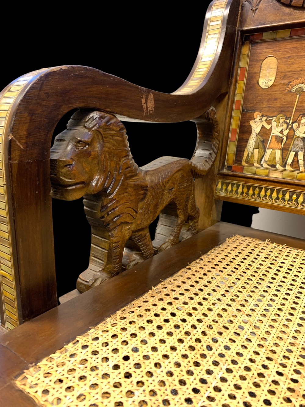 A three-piece nineteenth-century Egyptian Revival furniture suite consisting of a settee and two armchairs with carved winged crestings, figural marquetry backrests, and cane seats. View VIII