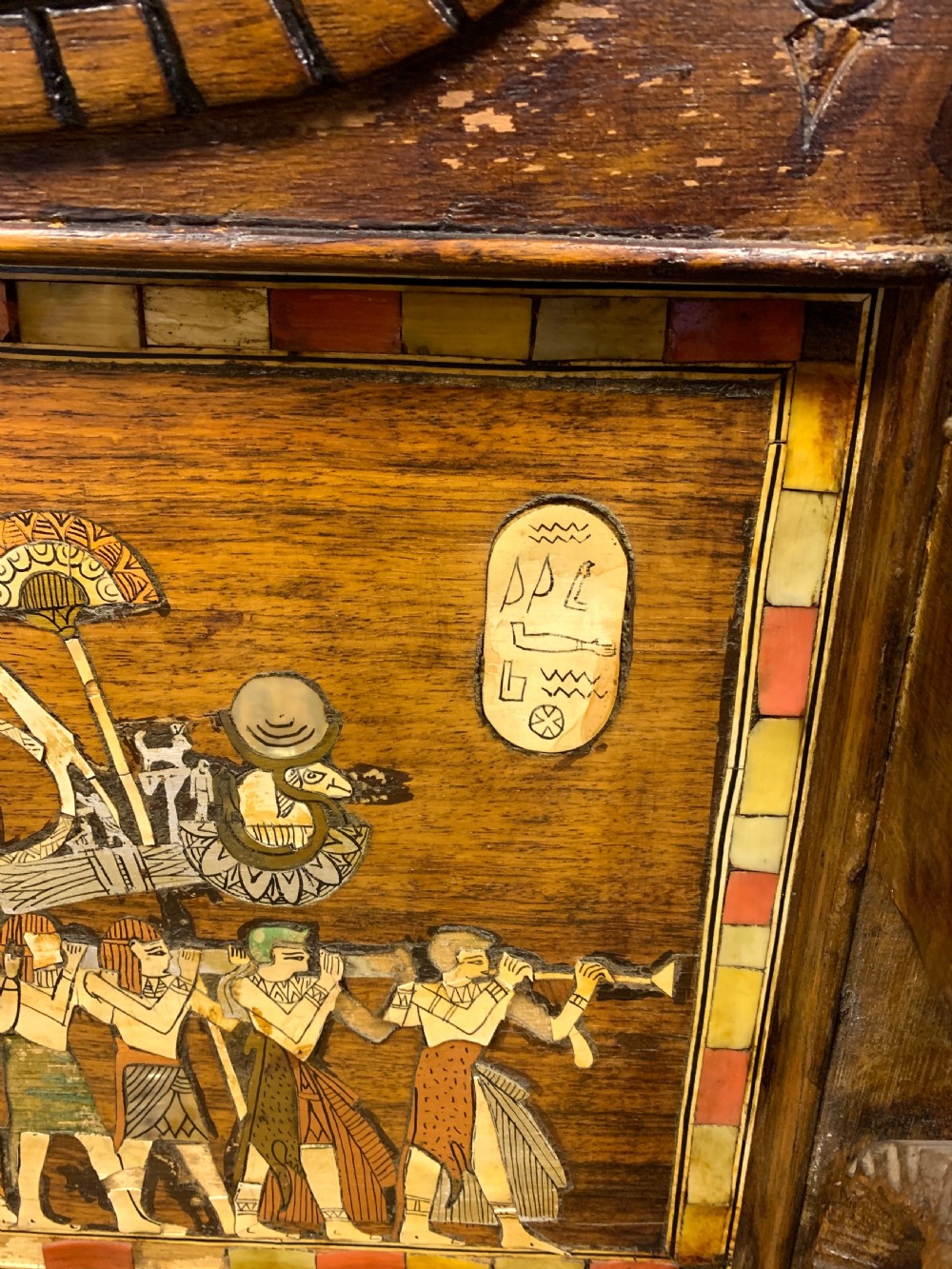 A three-piece nineteenth-century Egyptian Revival furniture suite consisting of a settee and two armchairs with carved winged crestings, figural marquetry backrests, and cane seats. View XIV