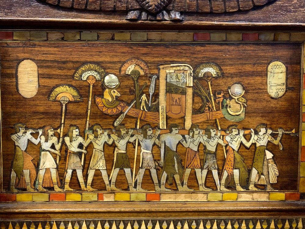 A three-piece nineteenth-century Egyptian Revival furniture suite consisting of a settee and two armchairs with carved winged crestings, figural marquetry backrests, and cane seats. View XVII