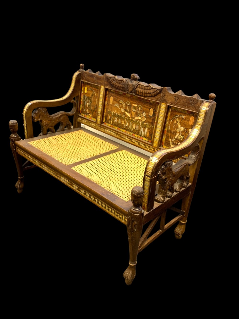 A three-piece nineteenth-century Egyptian Revival furniture suite consisting of a settee and two armchairs with carved winged crestings, figural marquetry backrests, and cane seats. View XVIII