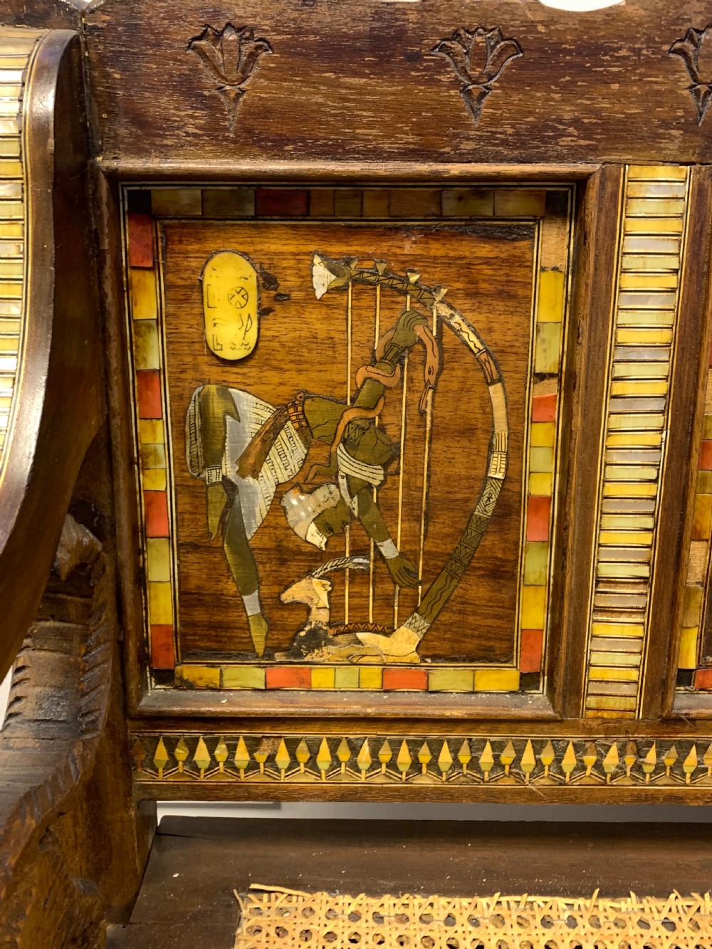 A three-piece nineteenth-century Egyptian Revival furniture suite consisting of a settee and two armchairs with carved winged crestings, figural marquetry backrests, and cane seats. View XX