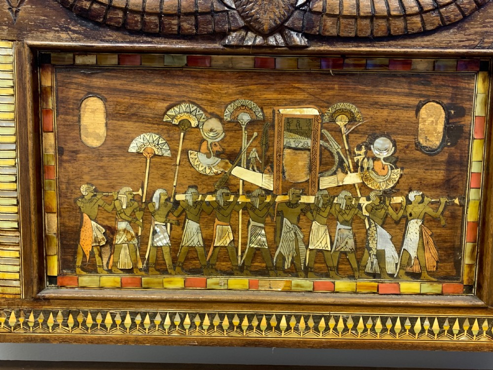 A three-piece nineteenth-century Egyptian Revival furniture suite consisting of a settee and two armchairs with carved winged crestings, figural marquetry backrests, and cane seats. View XXI