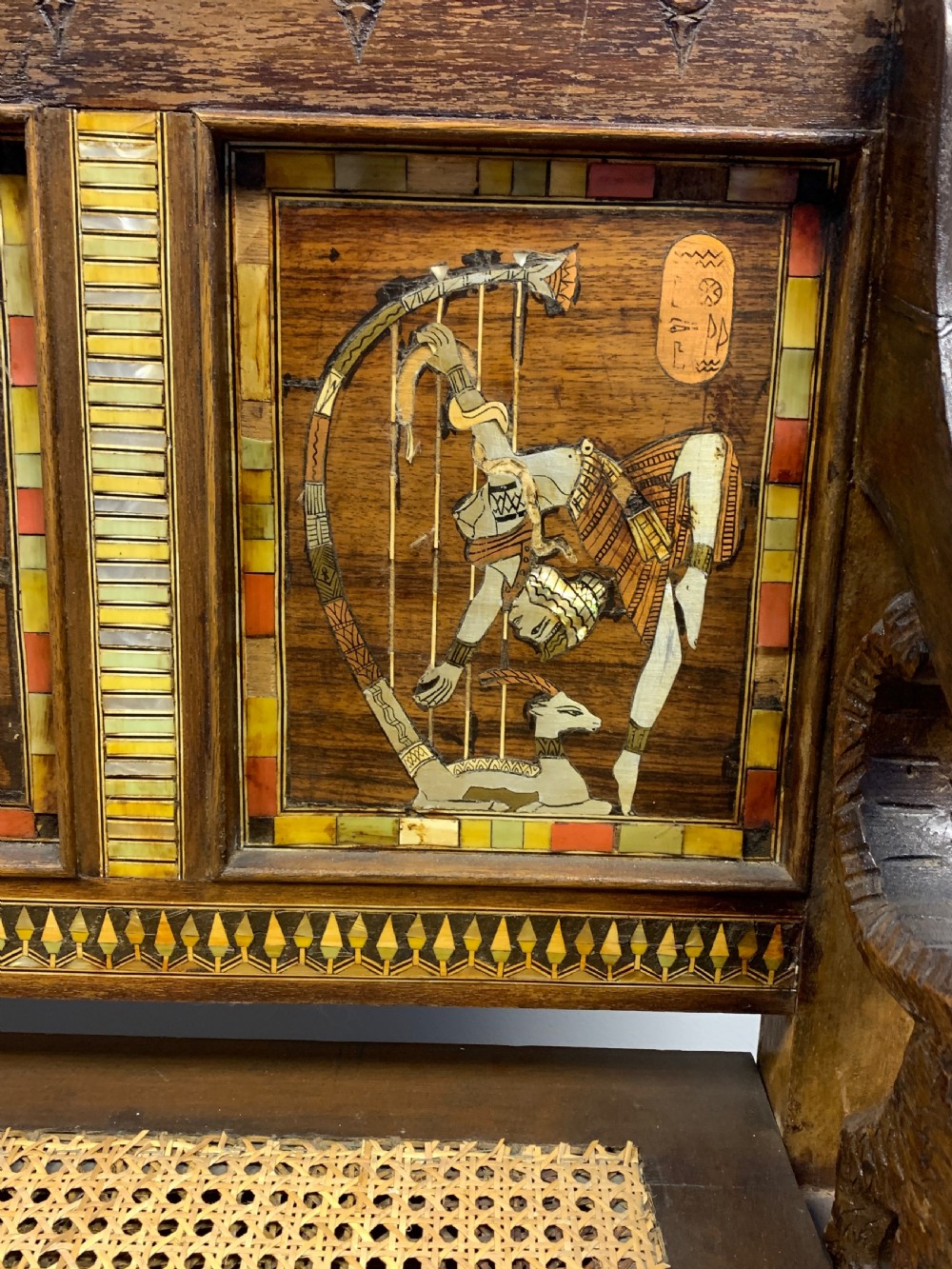 A three-piece nineteenth-century Egyptian Revival furniture suite consisting of a settee and two armchairs with carved winged crestings, figural marquetry backrests, and cane seats. View XXII