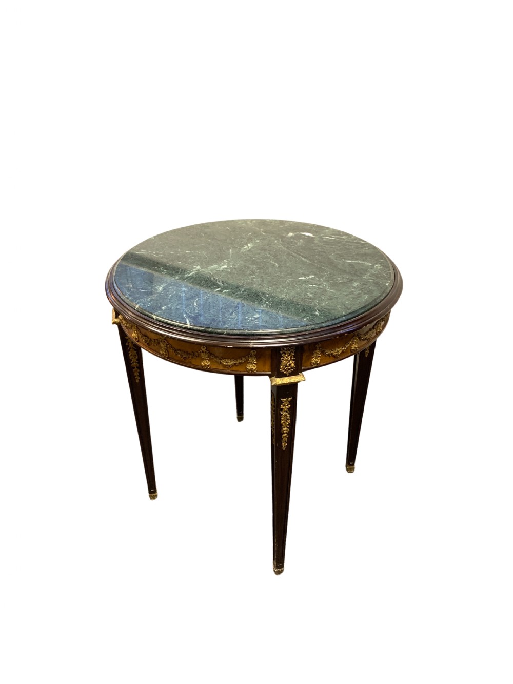 A circular centre table featuring a dark green marble top, a dark wooden apron embellished with gilt-bronze festoons, and four tapered legs with gold mounts.