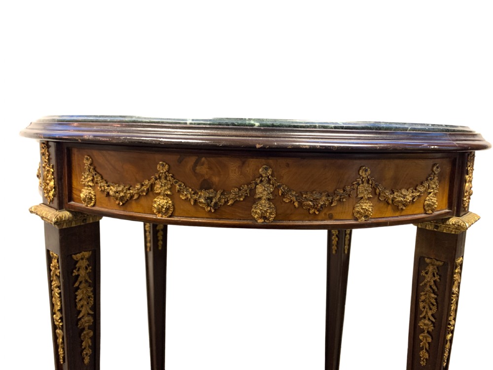 A circular centre table featuring a dark green marble top, a dark wooden apron embellished with gilt-bronze festoons, and four tapered legs with gold mounts. View III