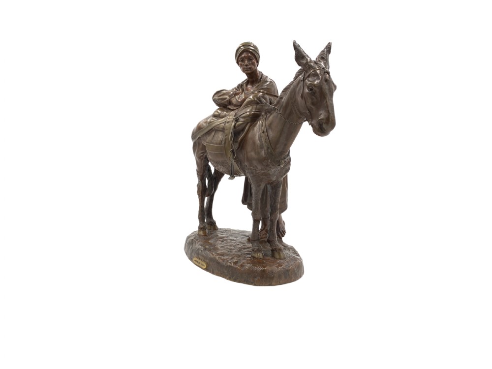 A dark patinated bronze sculpture featuring a man in traditional North African attire leaning against a saddled donkey on a naturalistic base with a title plaque. View II
