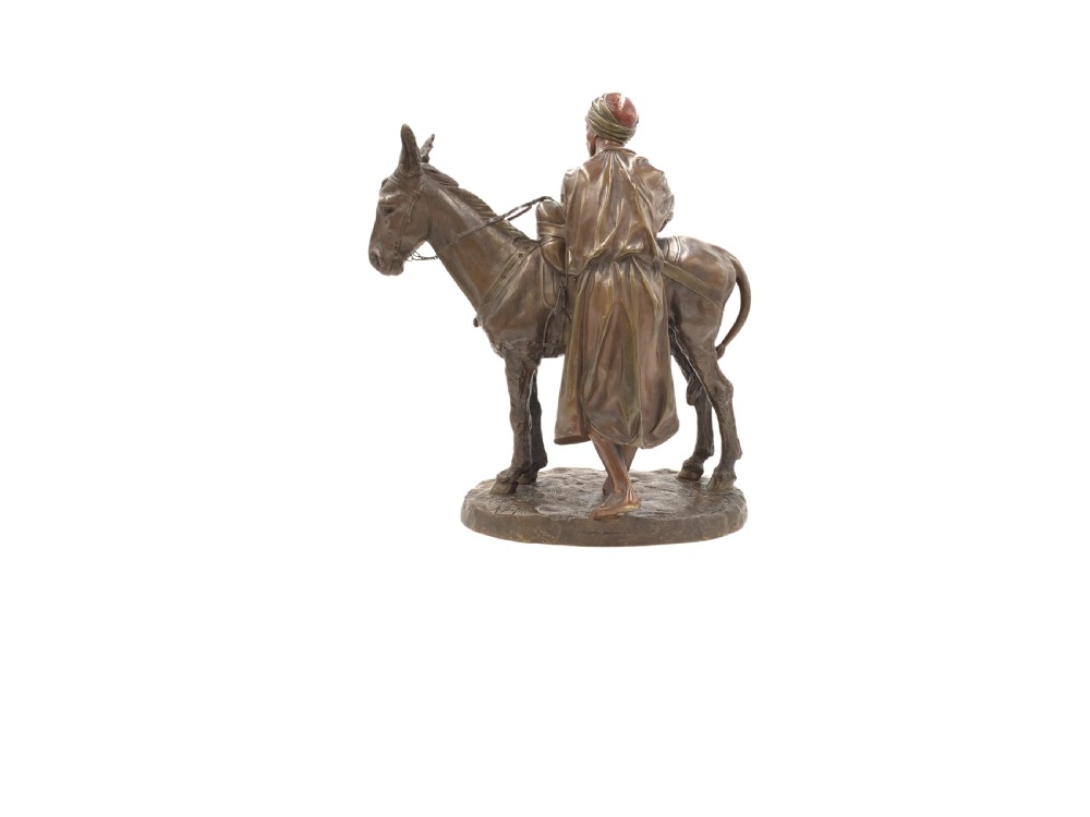 A dark patinated bronze sculpture featuring a man in traditional North African attire leaning against a saddled donkey on a naturalistic base with a title plaque. View III