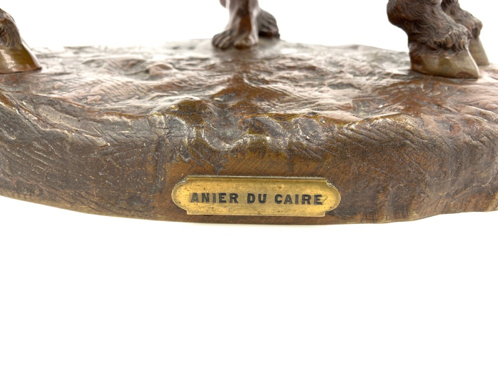A dark patinated bronze sculpture featuring a man in traditional North African attire leaning against a saddled donkey on a naturalistic base with a title plaque. View V