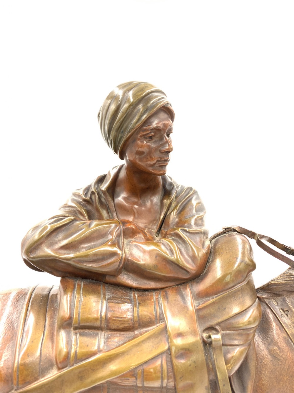 A dark patinated bronze sculpture featuring a man in traditional North African attire leaning against a saddled donkey on a naturalistic base with a title plaque. View VI
