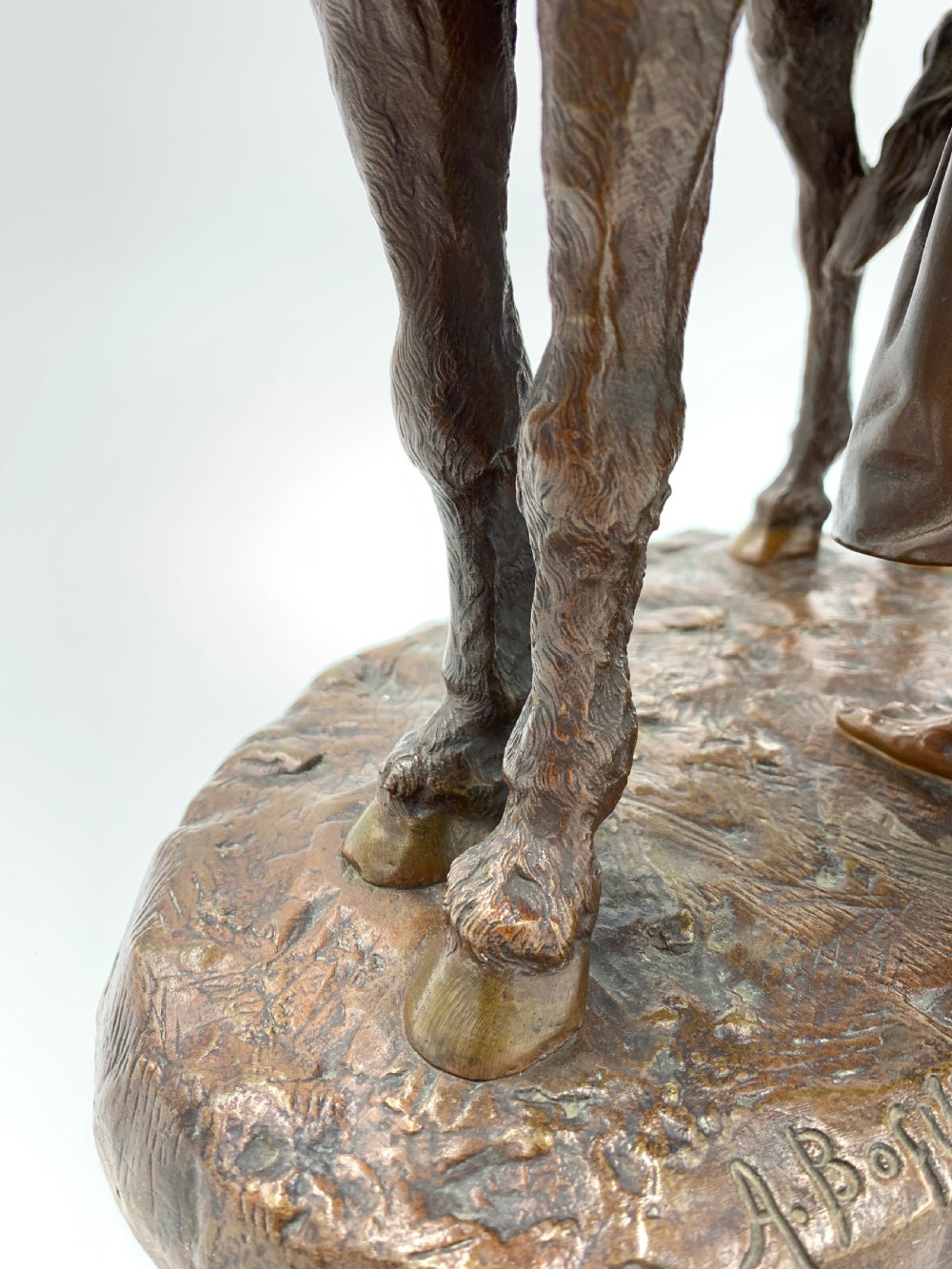 A dark patinated bronze sculpture featuring a man in traditional North African attire leaning against a saddled donkey on a naturalistic base with a title plaque. View IX