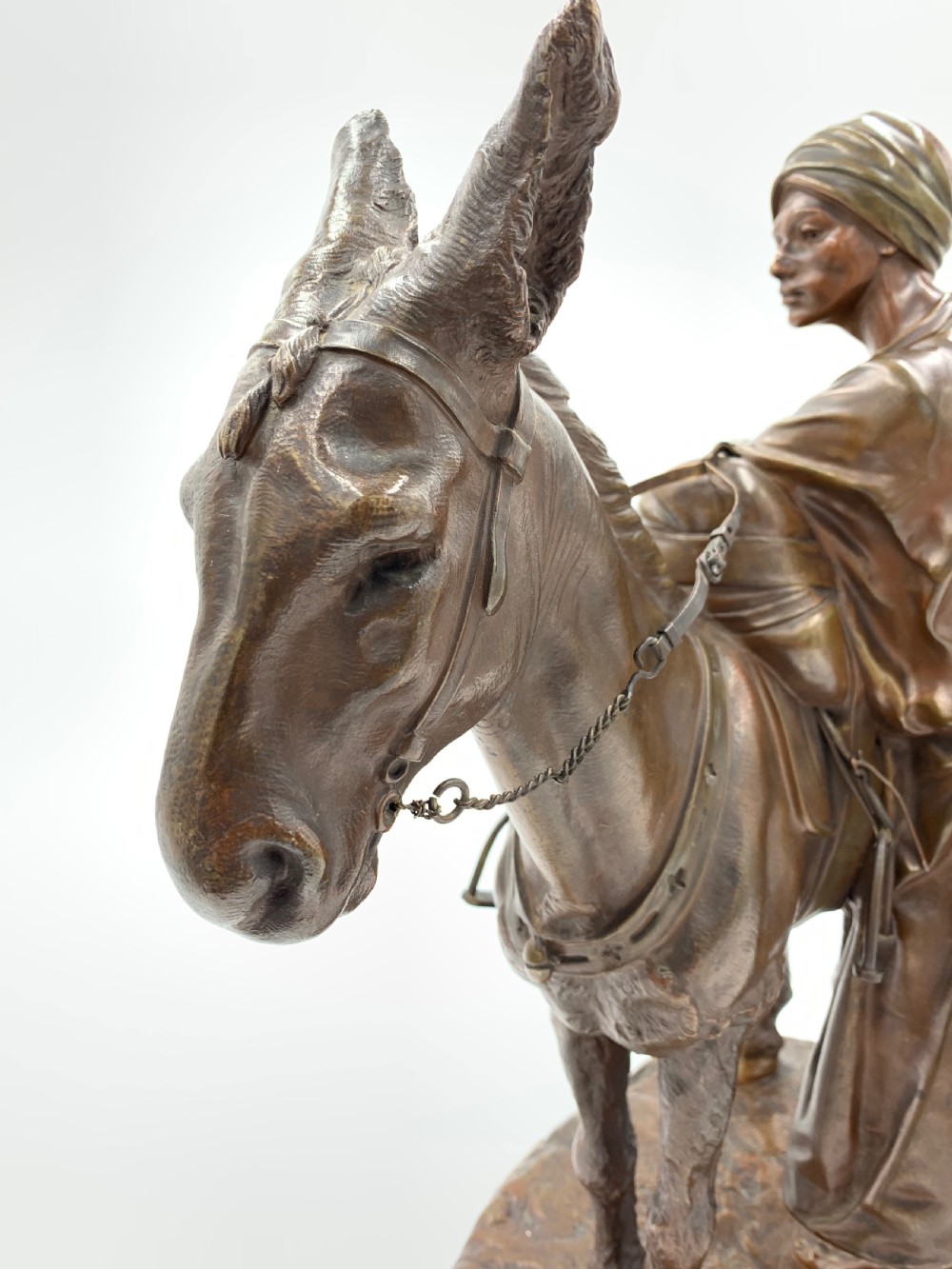 A dark patinated bronze sculpture featuring a man in traditional North African attire leaning against a saddled donkey on a naturalistic base with a title plaque. View X