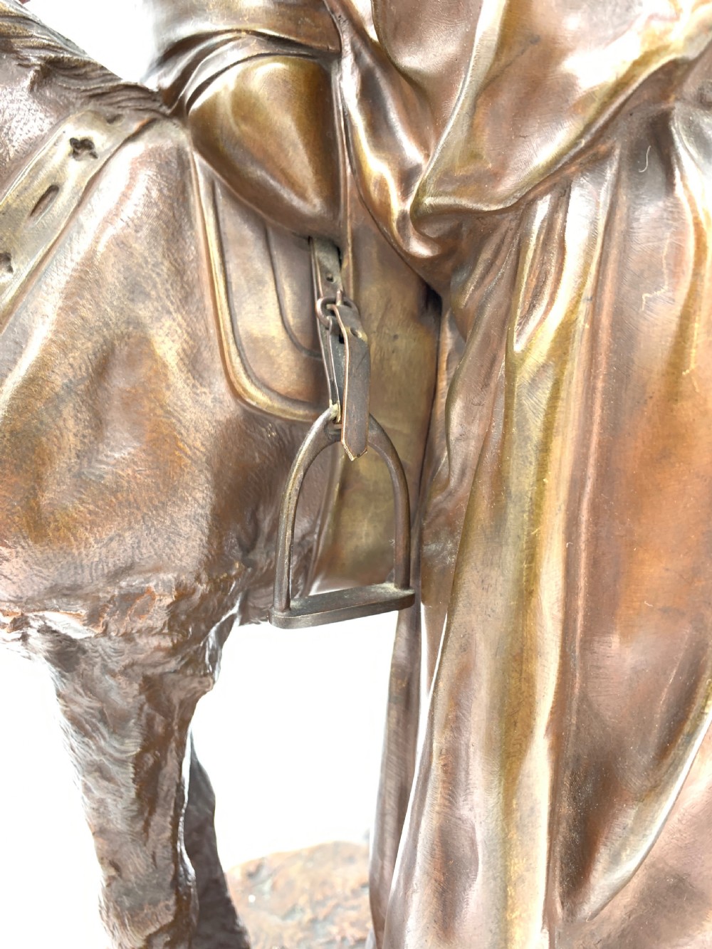 A dark patinated bronze sculpture featuring a man in traditional North African attire leaning against a saddled donkey on a naturalistic base with a title plaque. View XI