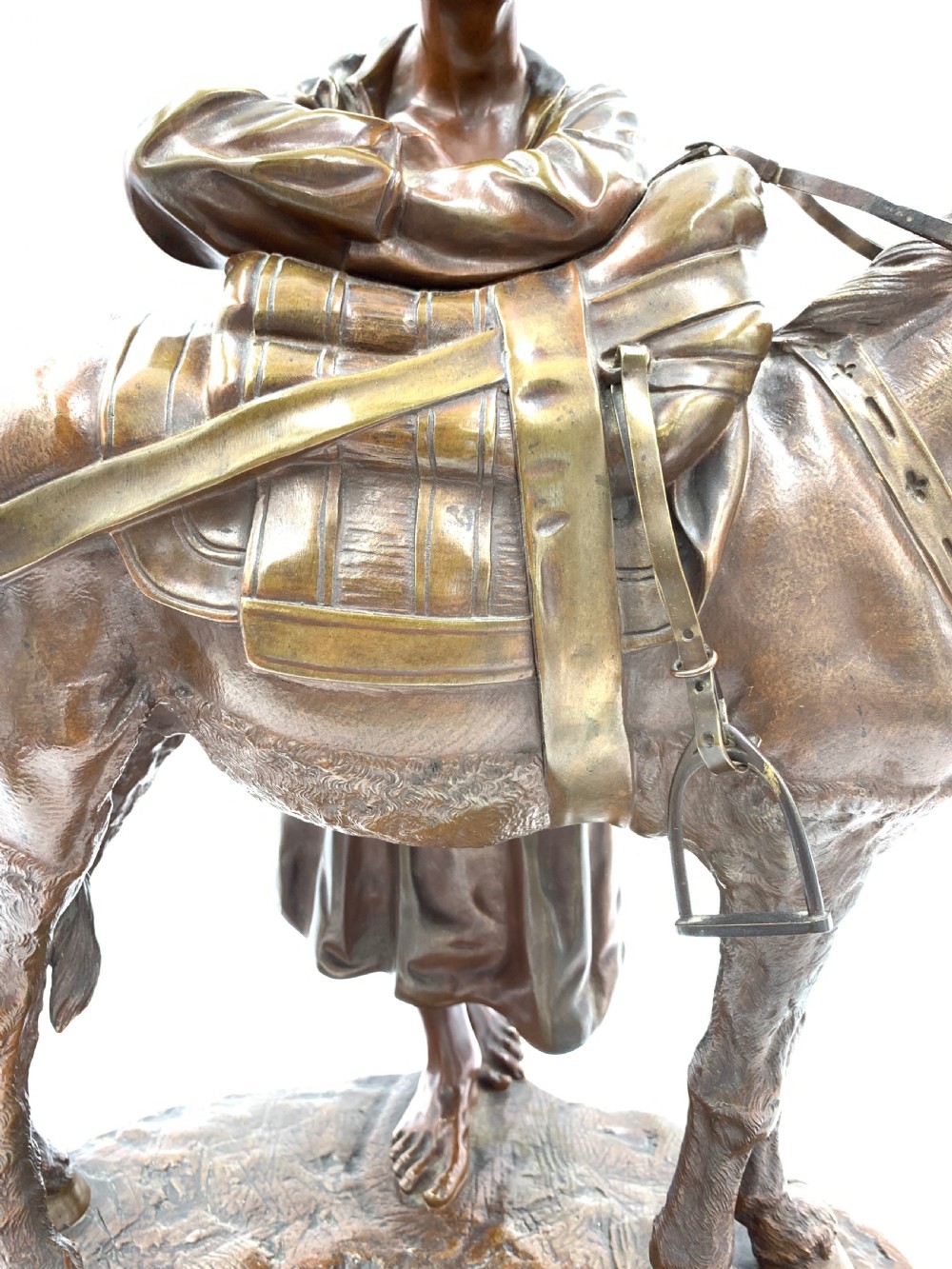 A dark patinated bronze sculpture featuring a man in traditional North African attire leaning against a saddled donkey on a naturalistic base with a title plaque. View XII