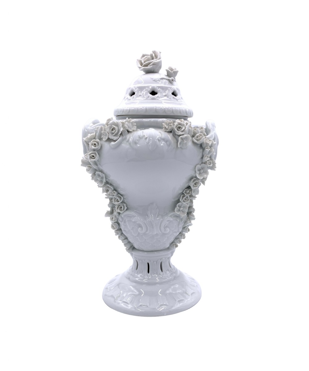 A white glazed porcelain urn featuring applied floral garlands, a pedestal base, and a pierced lid topped with a rose finial.