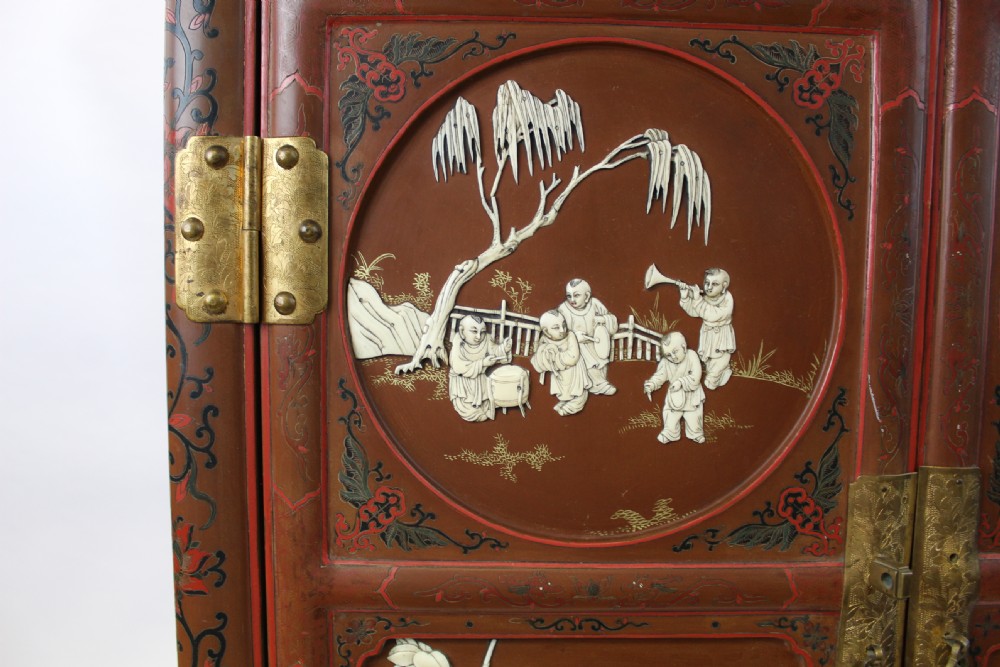 A 19th-century Chinese red lacquer cabinet featuring two doors decorated with carved white relief panels depicting figures, birds, and botanical motifs, fitted with brass lockplates. View VII