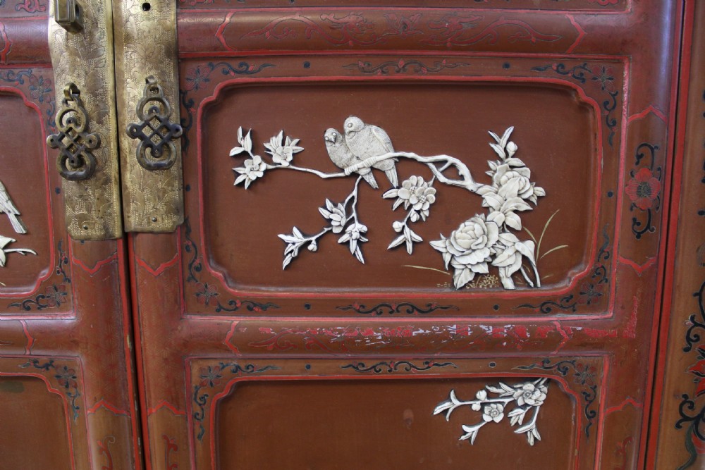 A 19th-century Chinese red lacquer cabinet featuring two doors decorated with carved white relief panels depicting figures, birds, and botanical motifs, fitted with brass lockplates. View VIII