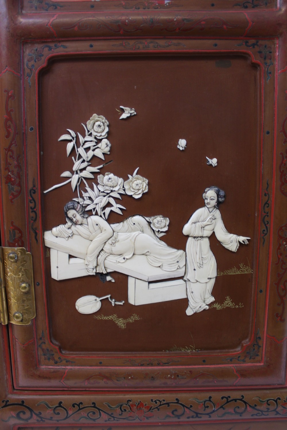 A 19th-century Chinese red lacquer cabinet featuring two doors decorated with carved white relief panels depicting figures, birds, and botanical motifs, fitted with brass lockplates. View XI