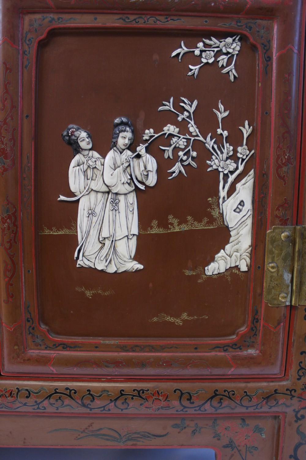 A 19th-century Chinese red lacquer cabinet featuring two doors decorated with carved white relief panels depicting figures, birds, and botanical motifs, fitted with brass lockplates. View XII