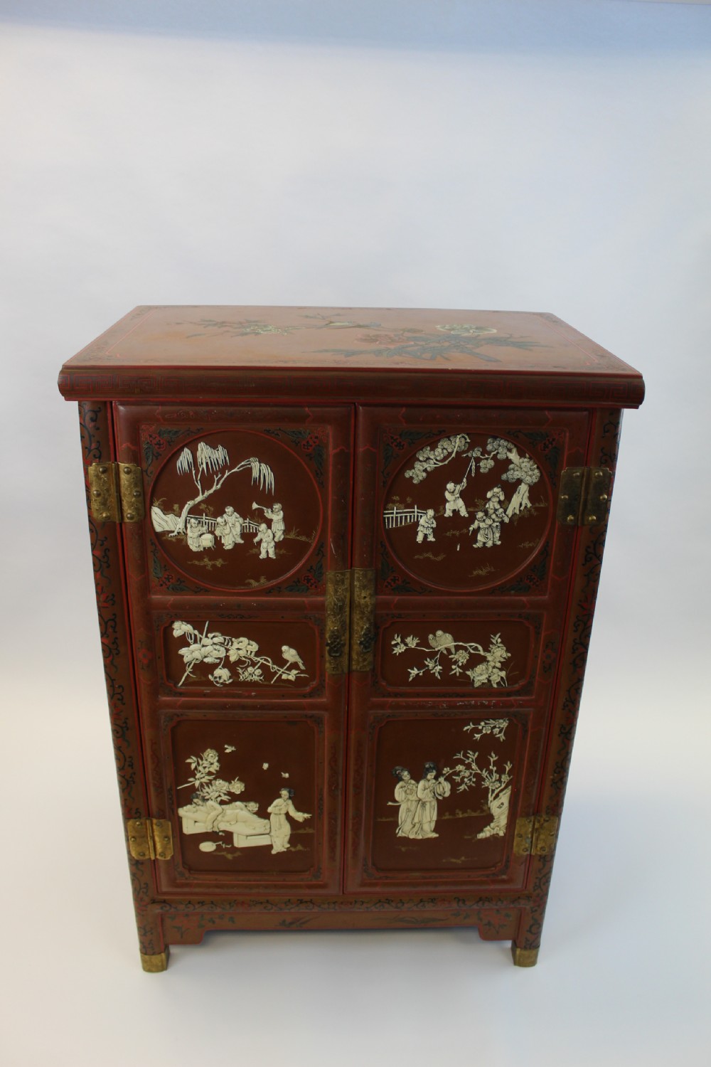 A 19th-century Chinese red lacquer cabinet featuring two doors decorated with carved white relief panels depicting figures, birds, and botanical motifs, fitted with brass lockplates. View XV