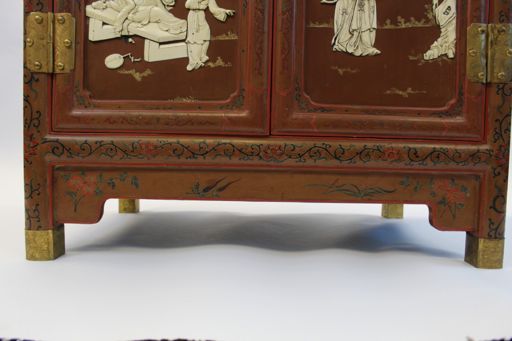 A 19th-century Chinese red lacquer cabinet featuring two doors decorated with carved white relief panels depicting figures, birds, and botanical motifs, fitted with brass lockplates. View XVII