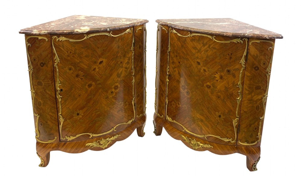 A matching pair of 19th-century French corner cabinets featuring floral marquetry panels, curved doors, gilt bronze mounts, and red-brown marble tops.