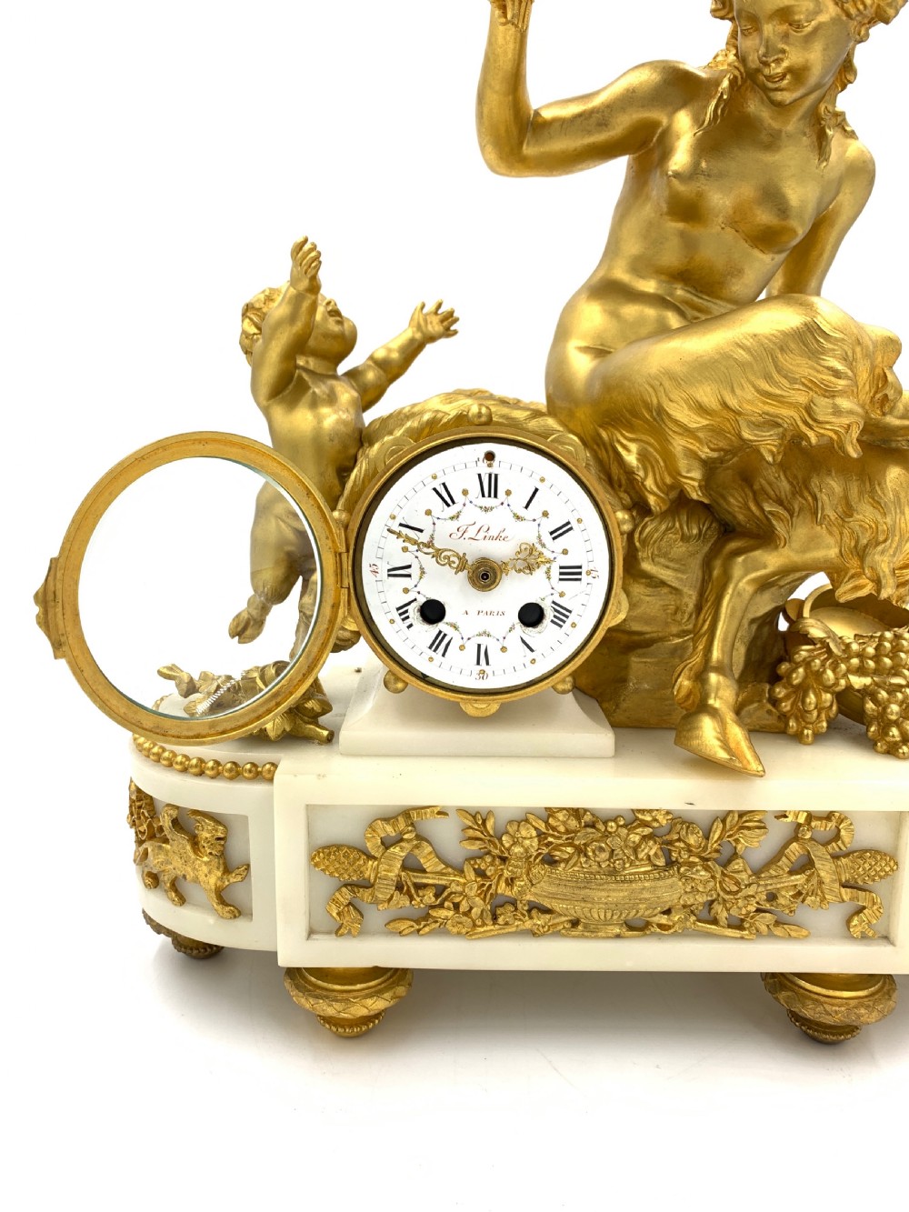 A late nineteenth-century French Louis XVI style gilt-bronze and white marble mantel clock featuring a sculptural bacchante figure alongside an enamel dial. View V