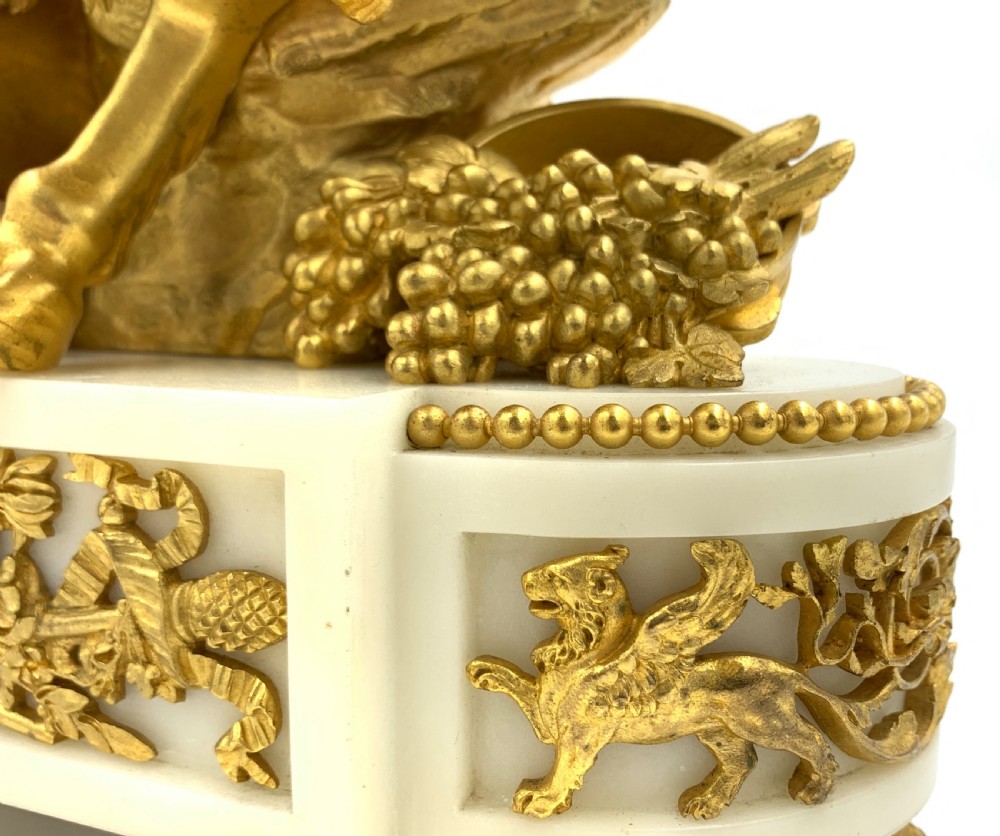 A late nineteenth-century French Louis XVI style gilt-bronze and white marble mantel clock featuring a sculptural bacchante figure alongside an enamel dial. View XII