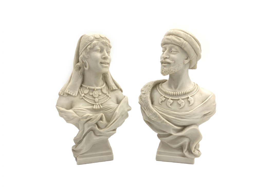 A pair of carved off-white marble busts depicting a man and woman in detailed Orientalist dress and headwear on integral square bases.