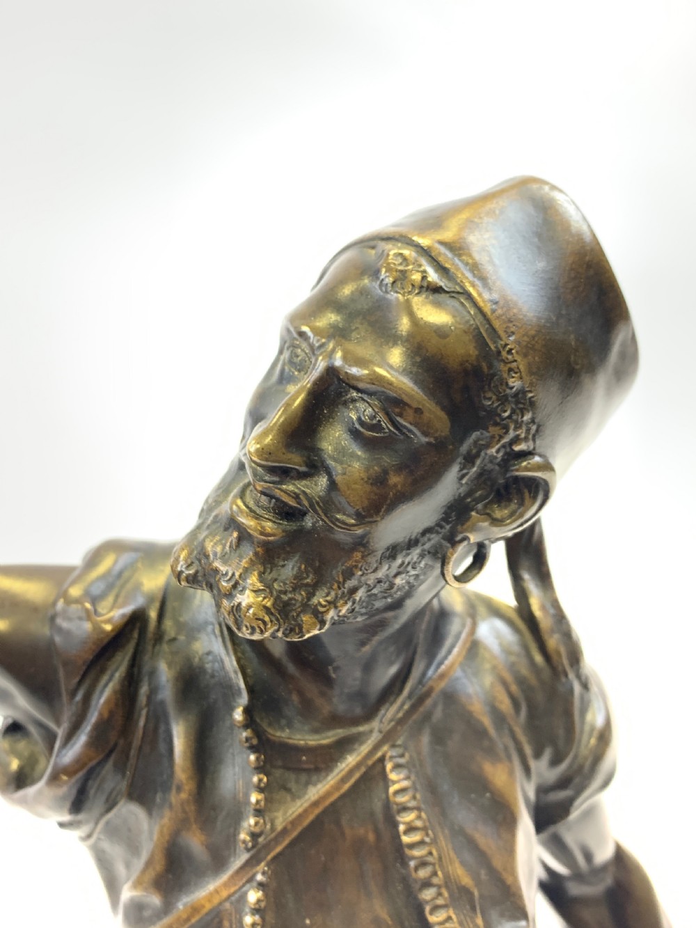 A dark brown patinated bronze sculpture depicting an Arab falconer holding a falcon overhead while standing on a circular base. View V