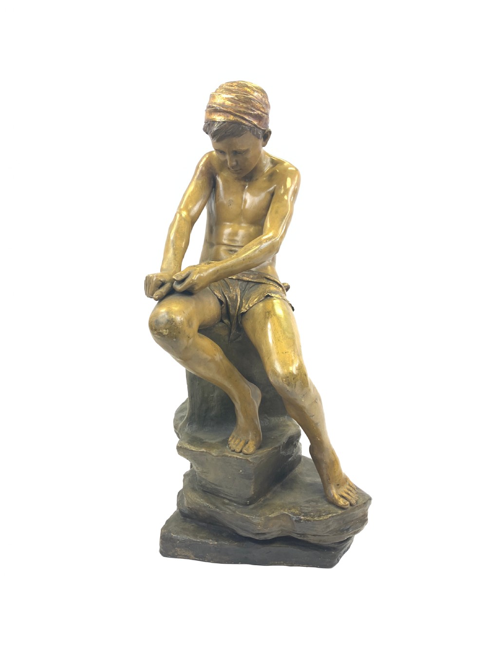 A late 19th-century Goldscheider cold-painted terracotta figure depicting a seated boy with a headscarf on a rocky base, finished in a bronzed metallic glaze.