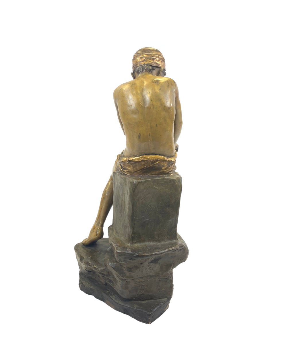 A late 19th-century Goldscheider cold-painted terracotta figure depicting a seated boy with a headscarf on a rocky base, finished in a bronzed metallic glaze. View III