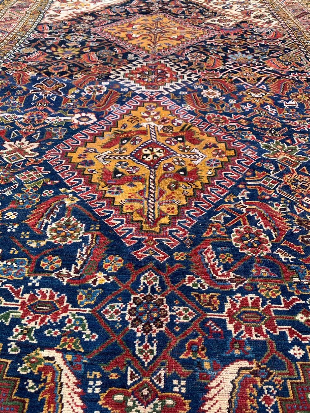 An antique Persian Qashqai hand-knotted wool rug featuring geometric diamond medallions on a navy blue tribal field with intricate multi-tiered borders. View V
