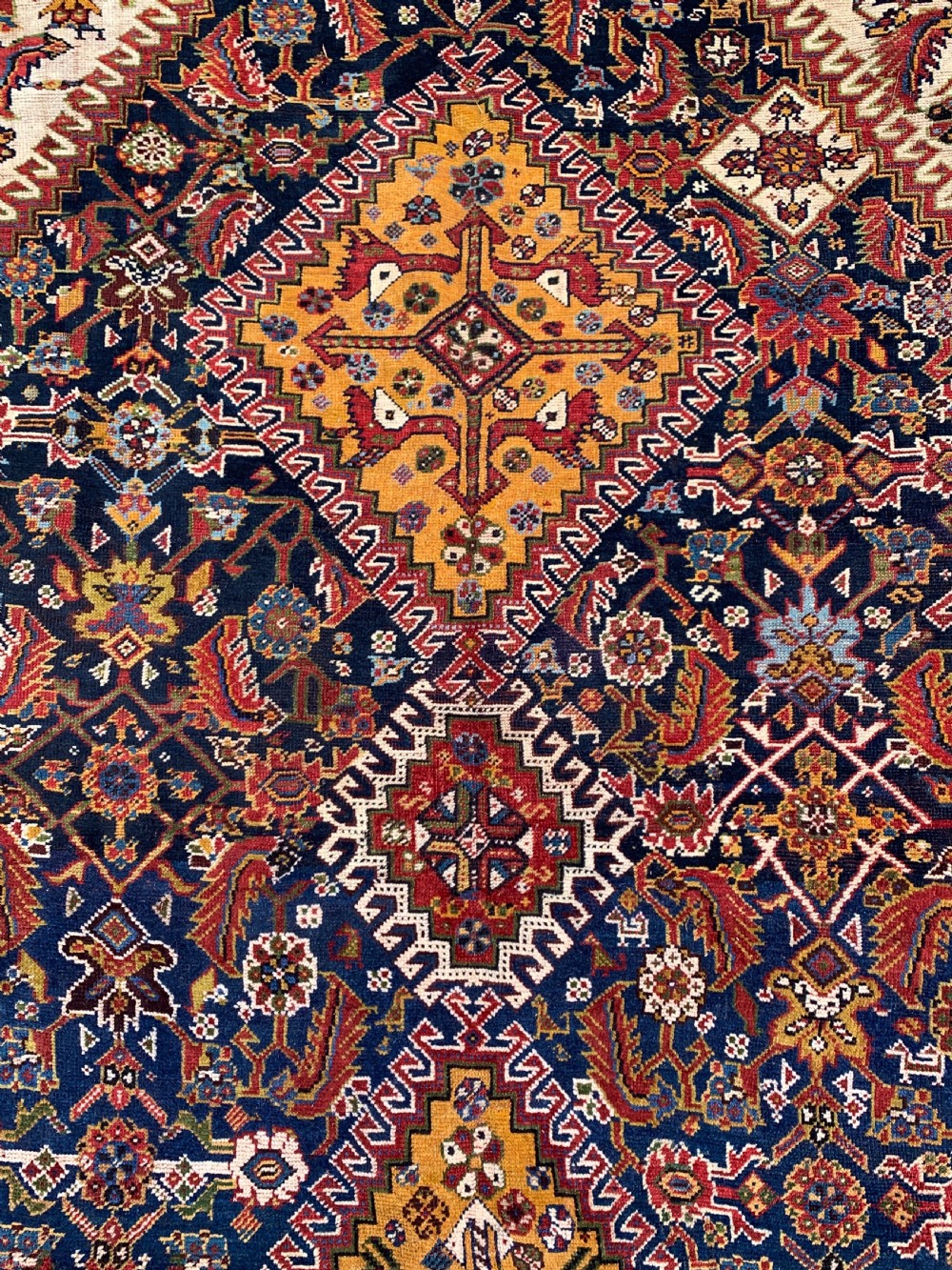 An antique Persian Qashqai hand-knotted wool rug featuring geometric diamond medallions on a navy blue tribal field with intricate multi-tiered borders. View VII