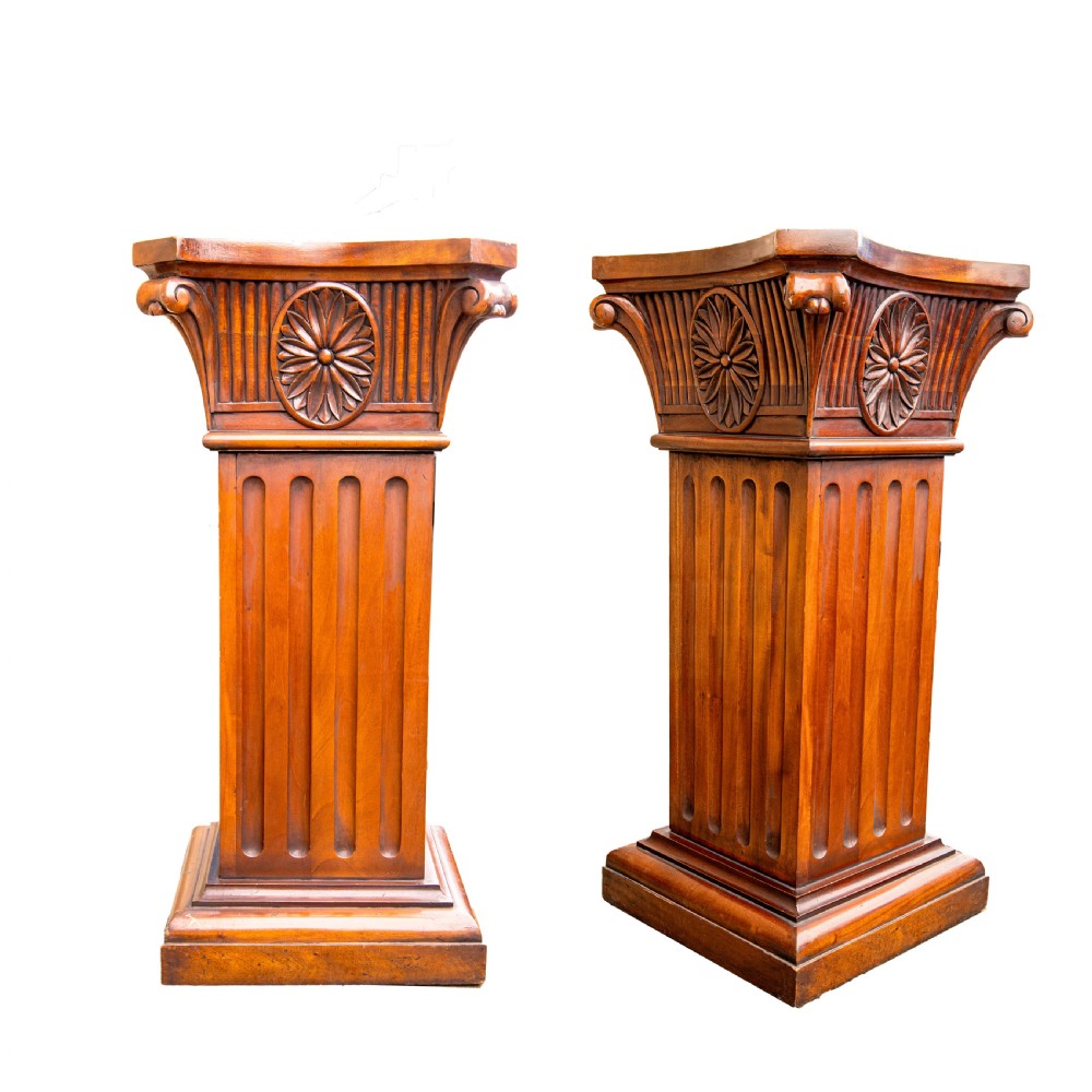 A pair of warm brown carved wooden pedestals featuring fluted shafts, ionic volutes, carved floral rosettes, and stepped square bases.