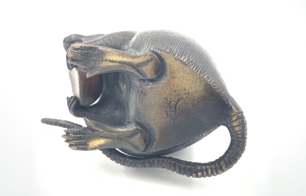 A dark bronze Japanese okimono sculpture depicting a rat sitting upright and clutching a chestnut. View IV