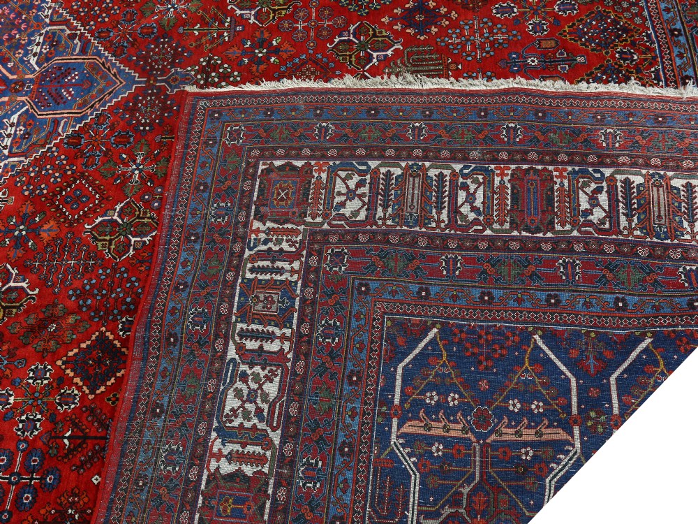 A large hand-knotted Persian Joshagan carpet featuring a central diamond medallion, intricate red geometric field, navy spandrels, and decorative borders. View V