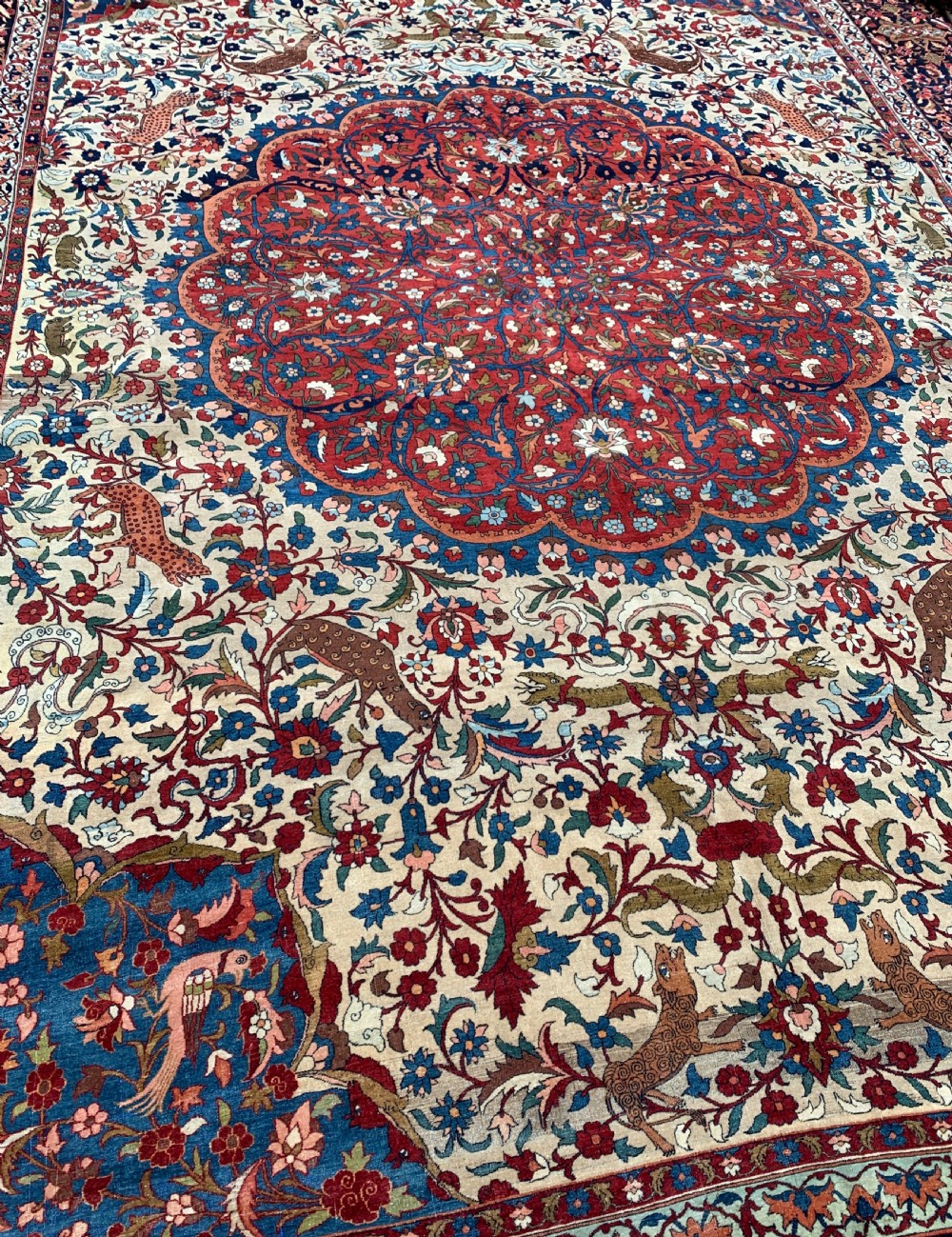 An antique Persian Isfahan wool carpet featuring a central red and blue medallion on an ivory field surrounded by detailed floral and animal patterns with a dark blue border. View IV
