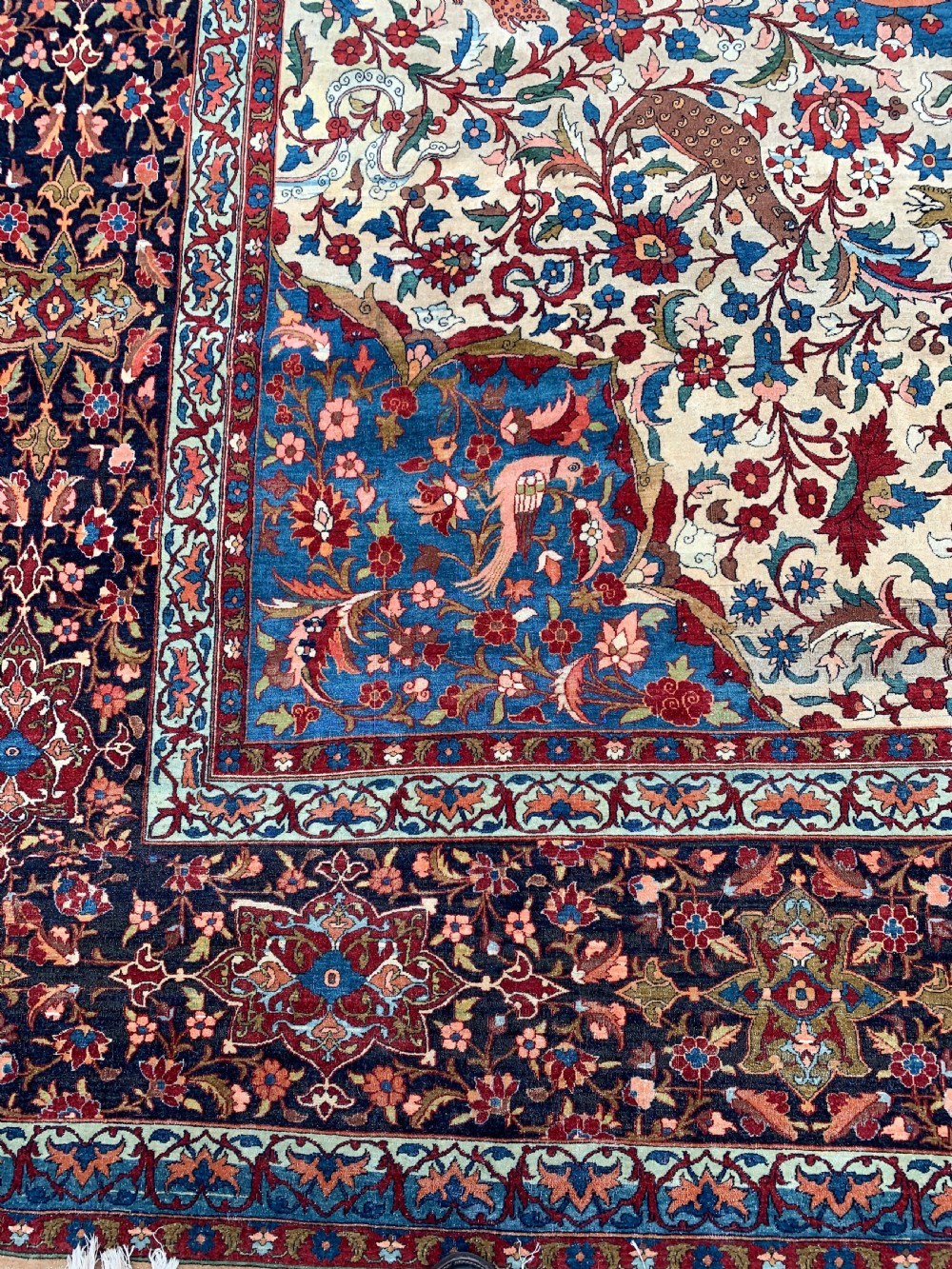 An antique Persian Isfahan wool carpet featuring a central red and blue medallion on an ivory field surrounded by detailed floral and animal patterns with a dark blue border. View VI
