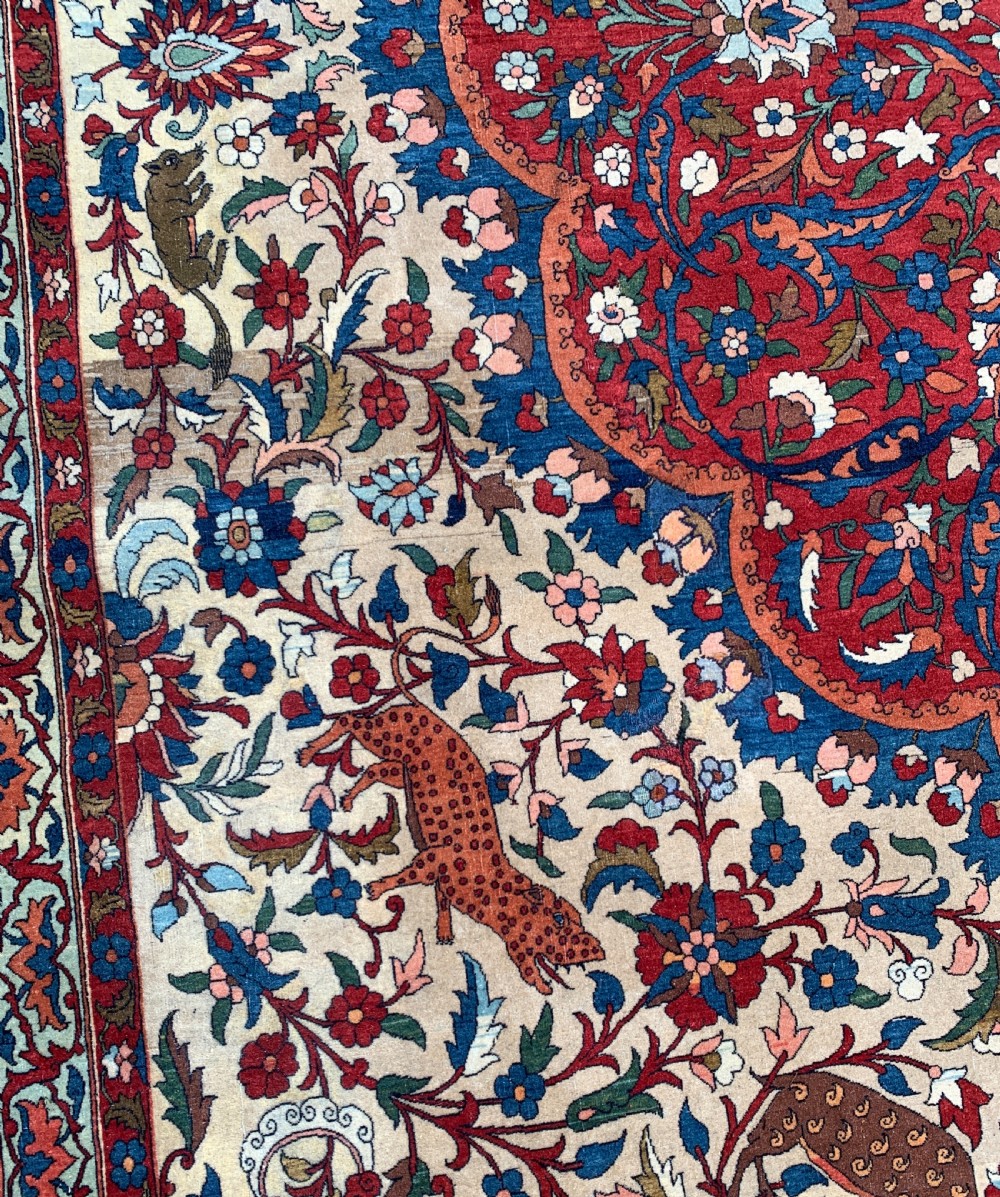 An antique Persian Isfahan wool carpet featuring a central red and blue medallion on an ivory field surrounded by detailed floral and animal patterns with a dark blue border. View VII