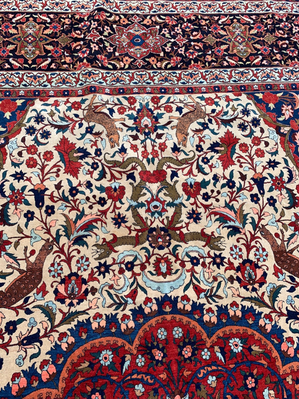 An antique Persian Isfahan wool carpet featuring a central red and blue medallion on an ivory field surrounded by detailed floral and animal patterns with a dark blue border. View VIII