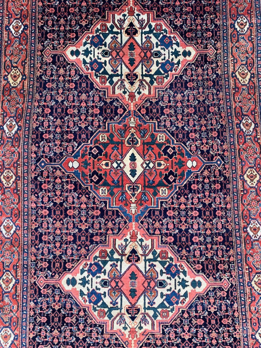 An antique Persian Senneh wool rug featuring three central diamond medallions set over a dark navy field with dense geometric floral motifs framed by a brick red border. View II