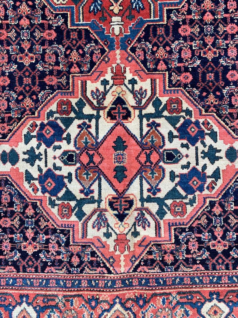 An antique Persian Senneh wool rug featuring three central diamond medallions set over a dark navy field with dense geometric floral motifs framed by a brick red border. View III