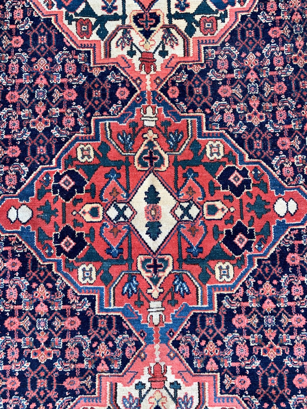 An antique Persian Senneh wool rug featuring three central diamond medallions set over a dark navy field with dense geometric floral motifs framed by a brick red border. View IV