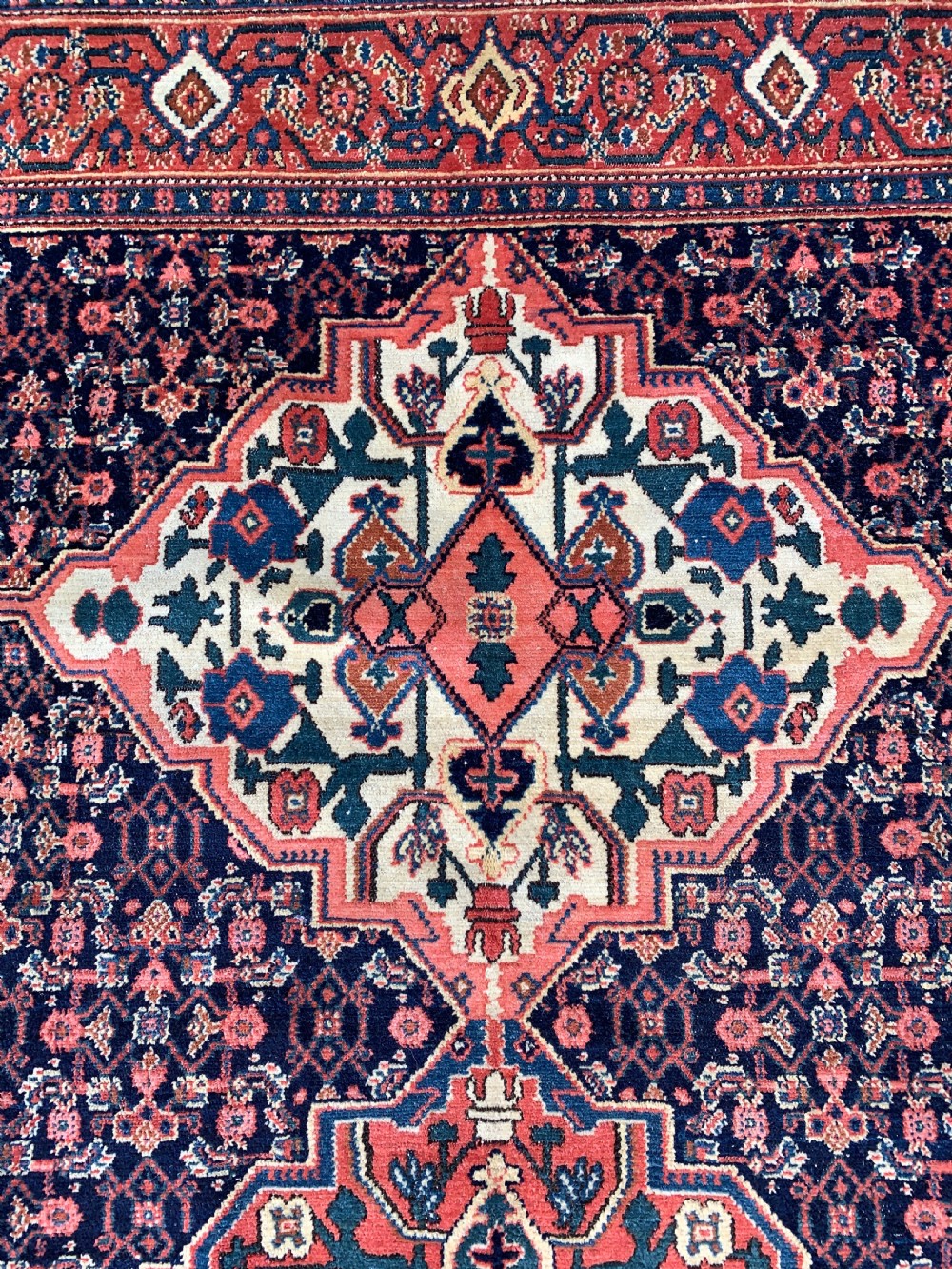 An antique Persian Senneh wool rug featuring three central diamond medallions set over a dark navy field with dense geometric floral motifs framed by a brick red border. View V