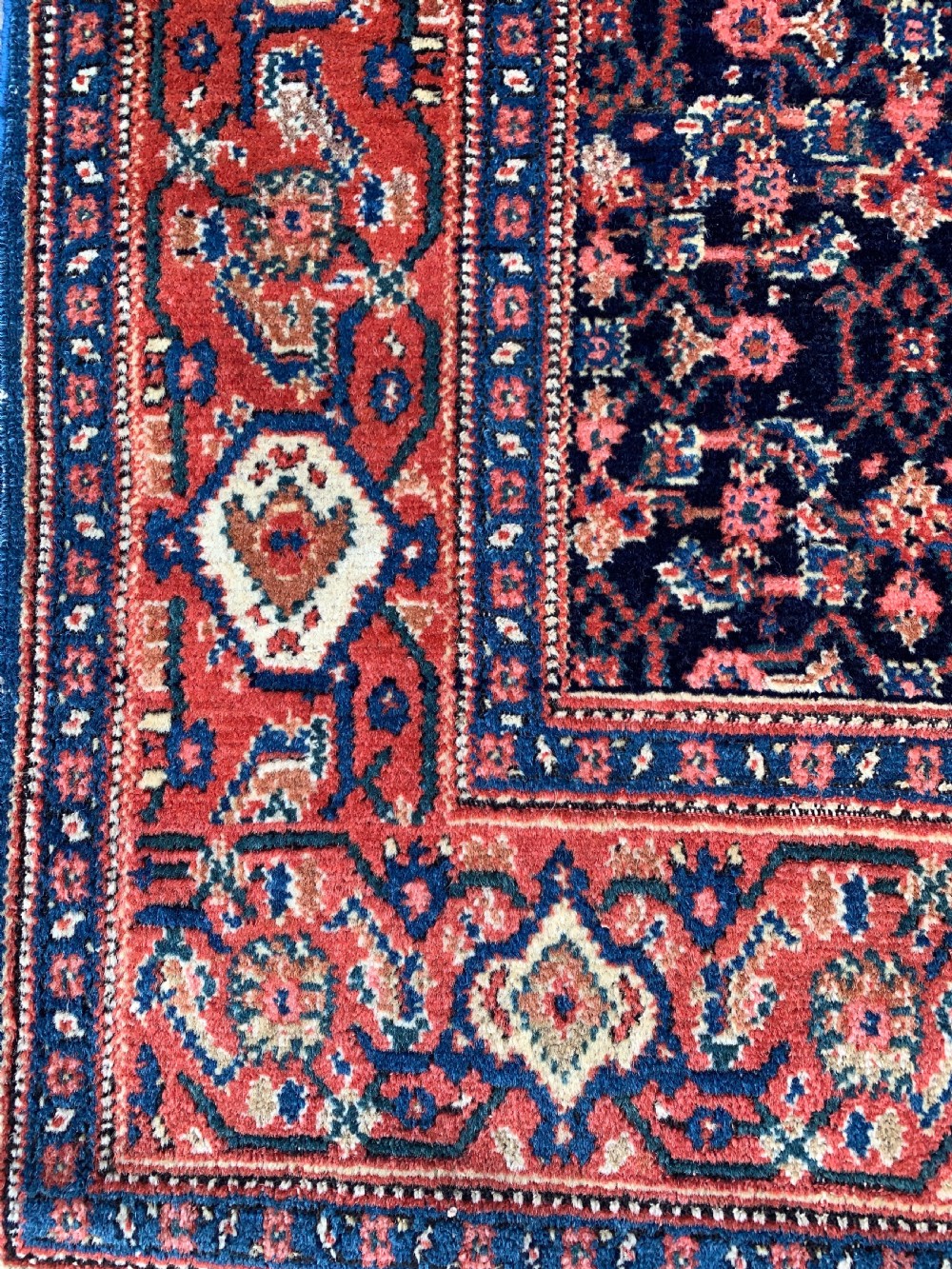 An antique Persian Senneh wool rug featuring three central diamond medallions set over a dark navy field with dense geometric floral motifs framed by a brick red border. View VI