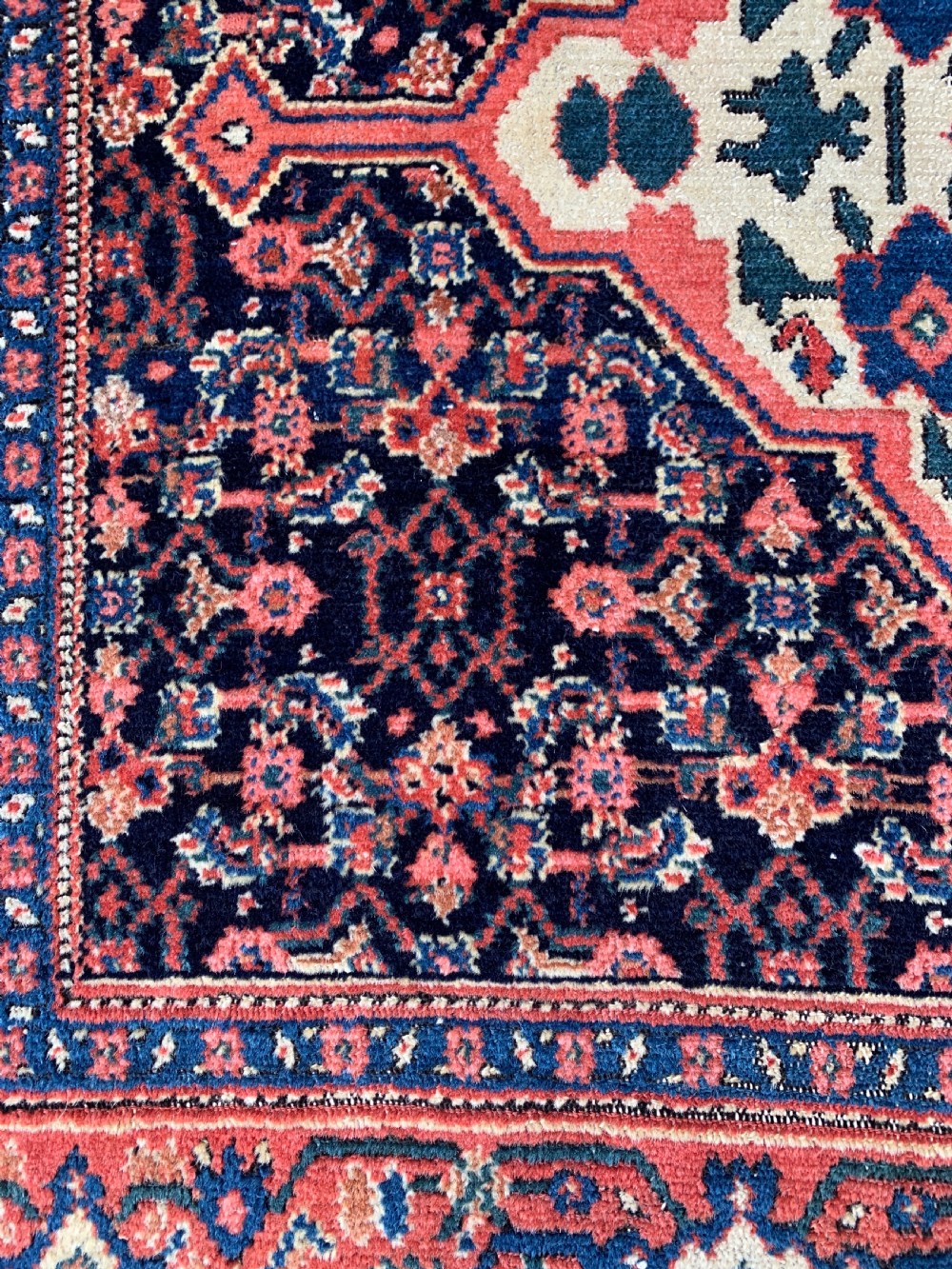 An antique Persian Senneh wool rug featuring three central diamond medallions set over a dark navy field with dense geometric floral motifs framed by a brick red border. View VII