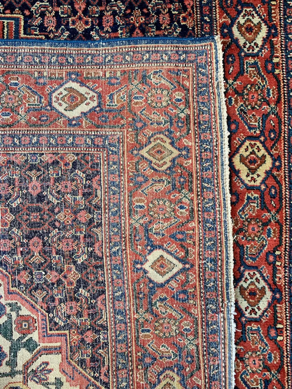 An antique Persian Senneh wool rug featuring three central diamond medallions set over a dark navy field with dense geometric floral motifs framed by a brick red border. View VIII