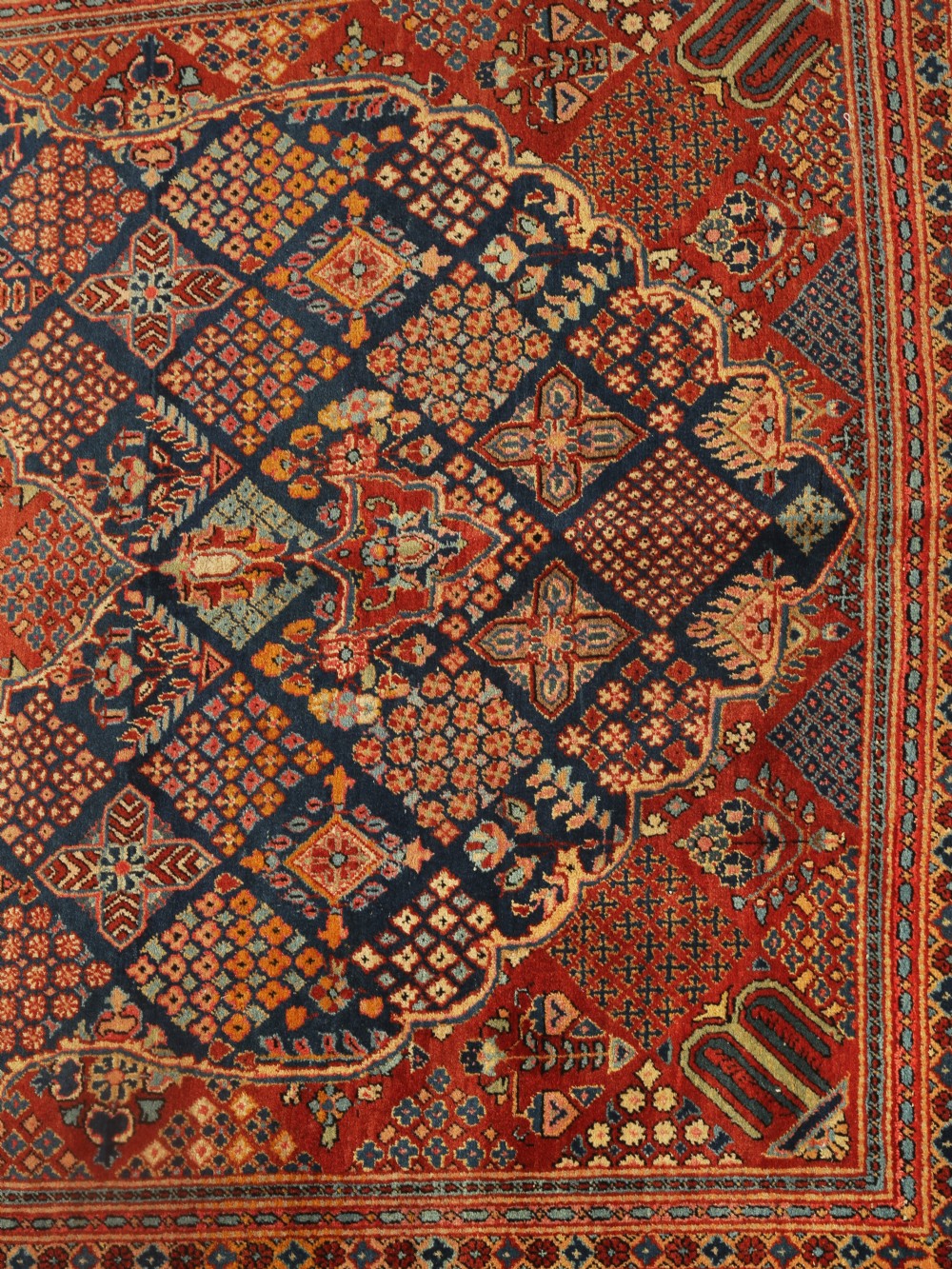 A rectangular Persian wool area rug featuring a central diamond medallion surrounded by intricate geometric lattice patterning in red, navy blue, and terracotta hues. View II