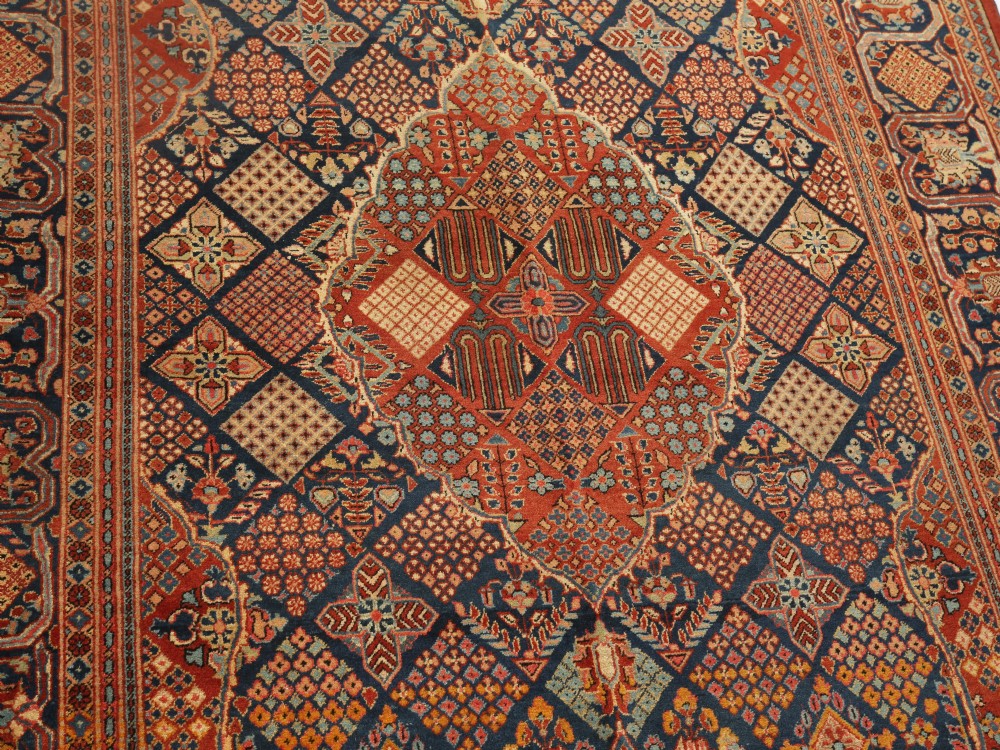 A rectangular Persian wool area rug featuring a central diamond medallion surrounded by intricate geometric lattice patterning in red, navy blue, and terracotta hues. View III